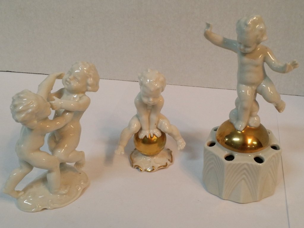 German Hutschenreuther Cherubs, 3 pcs.: A pair of wrestling cherubs, Hutschenreuther, appx. 4.5" tall. Together with a cherub on a gold ball, Hutschenreuther, 4". With a German cherub flower frog, appx. 6.5" tall.