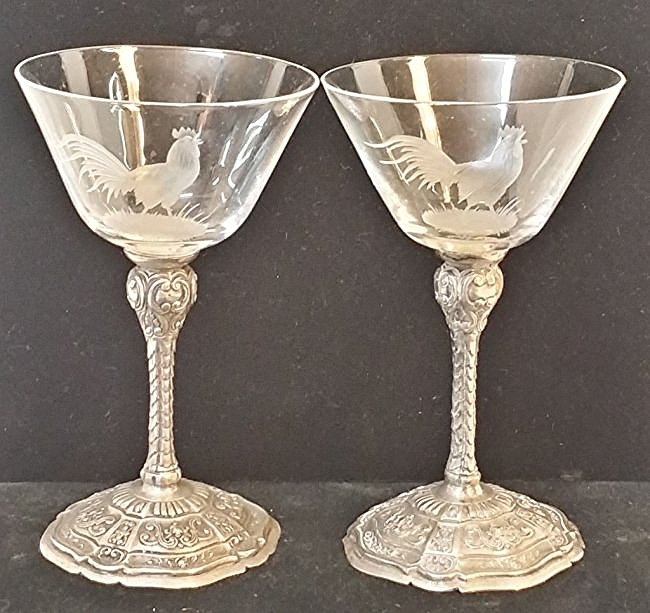 A pair of .800 silver cocktail glasses: A pair of silver and crystal cocktail glasses. The glass portion engraved with a etched rooster design. Bases marked with .800 silver marks.