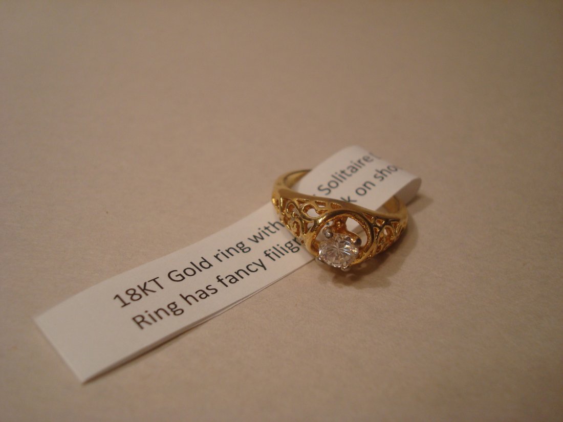 18K Gold Diamond ring, marked. 2.93 g: 18K Gold ring with clear solitaire diamond stone. It has fancy filigree work on shoulders with diamond stone on center. 18K Marked. 2.93 grams.