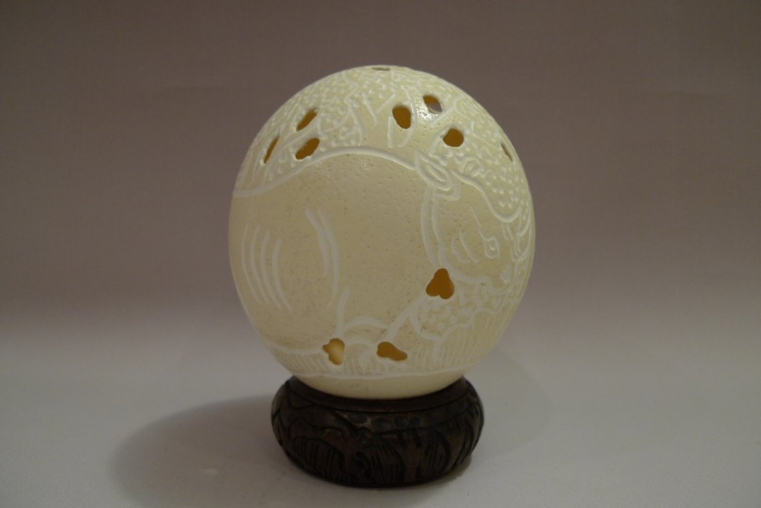 A HAND CARVED OSTRICH EGG W/ RHINO: A hand carved ostrich egg featuring rhino motif. Original hand carved base is included. W 5” x H 5.5” Provenance – From a Potomac, MD estate