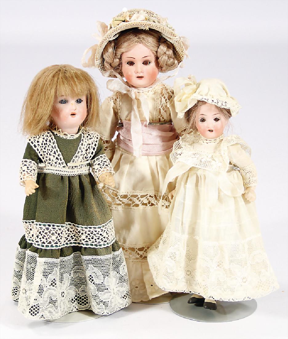 3 Porzellankopf-Puppen, 2x THEODOR RECKNAGEL, gem. DEP,: 3 Porzellankopf-Puppen, 2x THEODOR RECKNAGEL, gem. DEP, braune u. blaue fest eingesetzte Glasaugen, off. Mund, Zähne, 1x Kunsthaar- u. 1x Echthaar-Perücke, auf Masse-Stehkörper mit anmodell. Schuhe