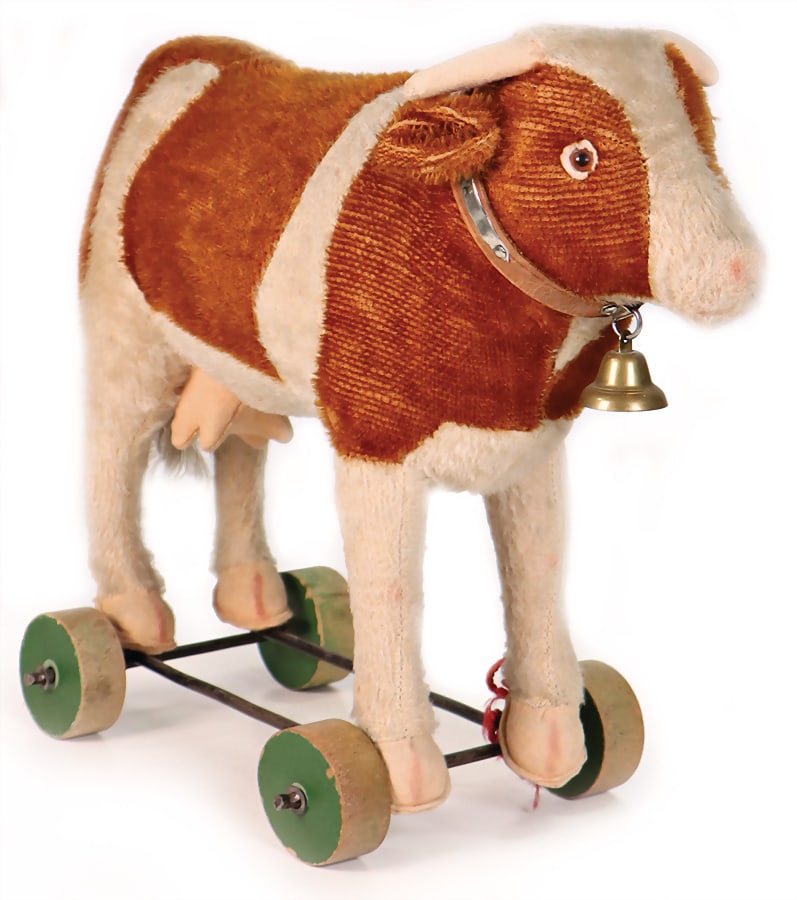 cow, on wooden wheels, brownish beige mohair, more worn in some parts, glass eyes underlaid with: cow, on wooden wheels, brownish beige mohair, more worn in some parts, glass eyes underlaid with felt, leather collar with bell, felt horns, as well as cow, on wooden wheels, mohair tail tip, with fel