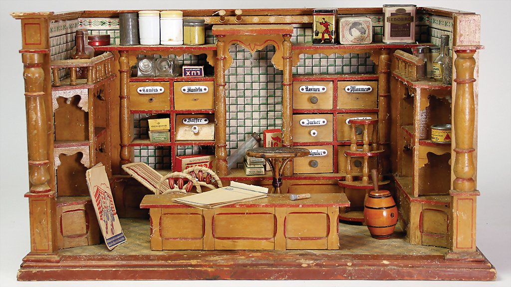 Kaufladen, um 1900, wohl Gottschalk, 59 cm breit, 33 cm: Kaufladen, um 1900, wohl Gottschalk, 59 cm breit, 33 cm hoch, alte Tapete, Tapete jedoch etwas jünger, mit Theke, ein paar Verzierungsteile sowie einige Schubladen fehlen, stark verunreinigt, schöne