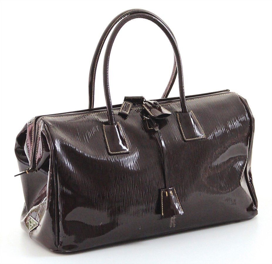 PRADA Damenhandtasche, pflaumenfarbenes Lackleder, ca.: PRADA Damenhandtasche, pflaumenfarbenes Lackleder, ca. 80er Jahre, 2 Tragehenkel, mittig 1 Anhänger mit 2 Schlüsseln, 1 Schloss im Leder-Etui, silberfarbene Prada-Plakette seitlich, 1 Fü