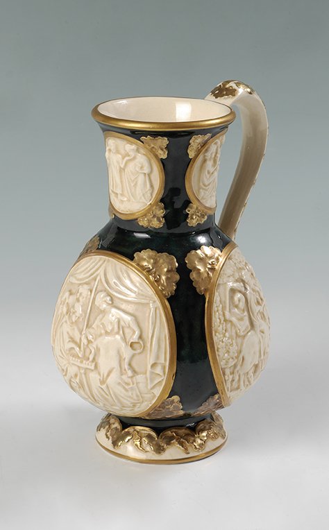 ZSOLNAY OLD IVORY POTTERY PITCHER: ZSOLNAY OLD IVORY POTTERY PITCHER: Rare "Old Ivory" with relief medallion of interior and exterior genre scenes, blue/green mottled ground, gilt foliate accents. 5 tower gilt mark, impressed 2966?, me