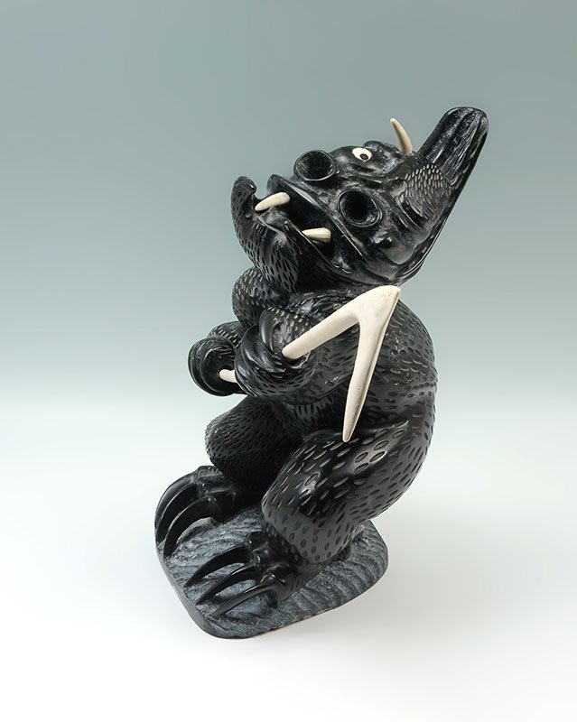 CHARLIE UGYUK CARVED KEEPER OF HUMANITY FIGURE: UGYUK, Charlie, (Canadian/Inuit, 1931-1998): Grotesque carved figure of an Inuit deity, referred to by the consigner as the "Keeper of Humanity". Hands and feet with claws, misshapen head with 3 bone 