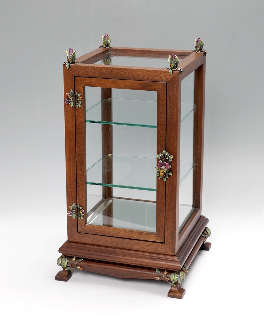JAY STRONGWATER DISPLAY CASE: JAY STRONGWATER DISPLAY CASE: Table top display case with enamel flower finials, hinged and door pull, glass on all 4 sides and top footed base with flower decoration continuing. Metal tag on back, ov