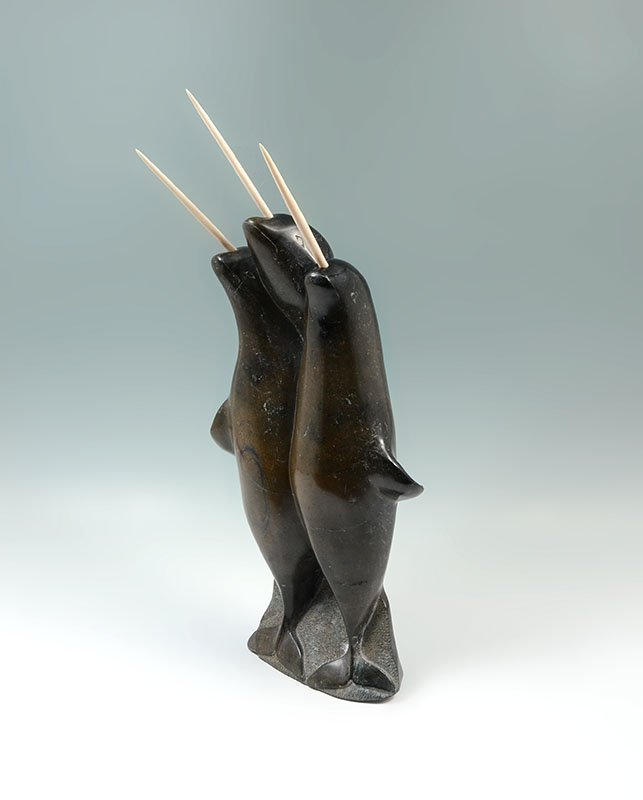 INUIT OSUITOK IPEELEE CARVED NARWHAL FIGURAL GROUP: INUIT CARVED STONE NARWHAL FIGURAL GROUP: Unsigned, original gallery tag identifies artist as Osuitok Ipeelee, circa 1975, carved stone group of 3 narwhal with bone "horns". Overall measures 20 3/4" h