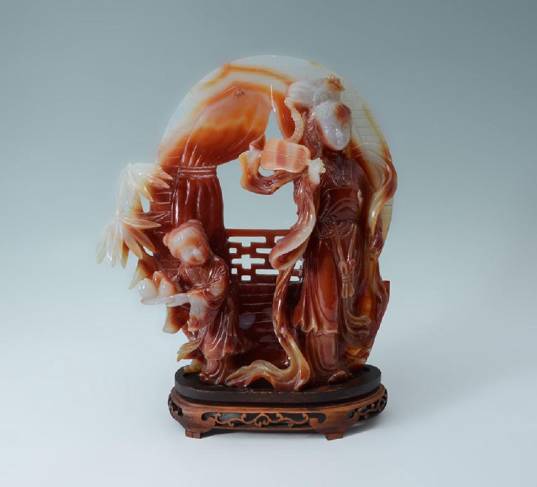CARVED CARNELIAN AGATE MOTHER & CHILD GROUP: CARVED CARNELIAN AGATE MOTHER & CHILD GROUP: Chinese relief carved carnelian agate figural group with maiden holding a fan and child holding a tray of fruit on flat pierced carved back, overall measur