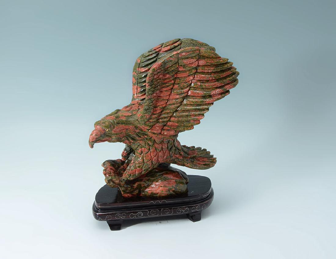 CARVED JASPER FIGURAL EAGLE: CARVED JASPER FIGURAL EAGLE: Chinese carved red and pink jasper or similar stone figure of an eagle, 8 1/4'' h x 7 3/4'' x 4 1/4''. Sold with a wood stand with silver wire, 1 1/2'' h. x 7 3/4'' x 4''.