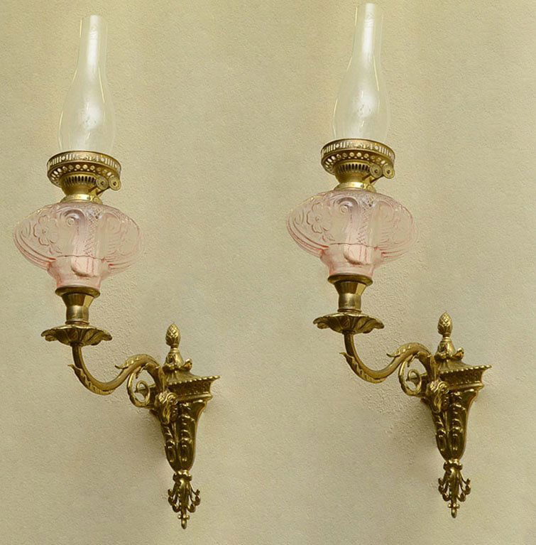 PAIR BRASS RAMS HEAD WALL OIL LAMP SCONCES: PAIR BRASS RAMS HEAD WALL OIL LAMP SCONCES: Victorian cast brass wall sconces with rams head holding single arm, embossed rose glass reservoir, double Duplex burner. Overall measures 20" h. x 6 3/4" x