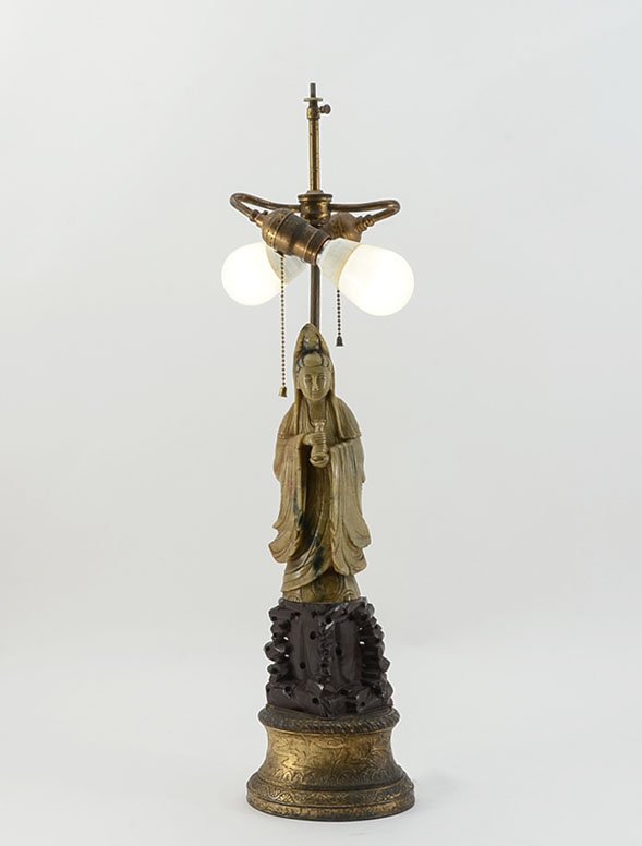 CARVED SOAPSTONE GUAN YIN FIGURAL LAMP: CARVED SOAPSTONE GUAN YIN FIGURAL LAMP: Figure of Guan Yin (alternate spellings Guanyin, Quan Yin, Kwan Yin) standing on a carved wood, above embossed gold decorated metal base. Double socket fixture,