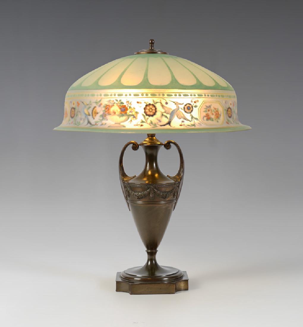 PAIRPOINT REVERSE PAINTED LAMP: PAIRPOINT REVERSE PAINTED LAMP: Patinated metal urn form base marked Pairpoint, D3016, 3 socket fixture, measures 25 1/4'' x 7 1/4''. Molded reverse painted shade with bird, floral and urn motif band,