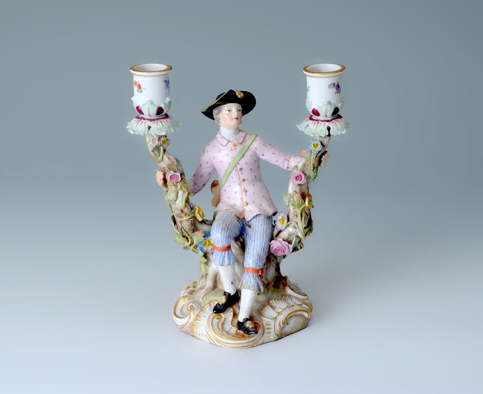 MEISSEN CHEVALIER PORCELAIN CANDLESTICK: MEISSEN CHEVALIER PORCELAIN CANDLESTICK: Modeled by J. J. Kaendler, 2 light candlestick with figural seated chevalier between 2 branches with applied flowers. Blue underglaze crossed swords marks, inc