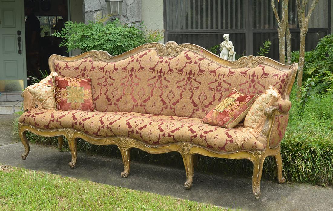 LARGE CONTINENTAL CARVED PARCEL GILT SOFA: LARGE CONTINENTAL CARVED PARCEL GILT SOFA: Carved giltwood frame in the rococo style, shaped top rail with foliate scroll, arms with fluted hand holds, carved and shaped skirt and legs, maroon and gol