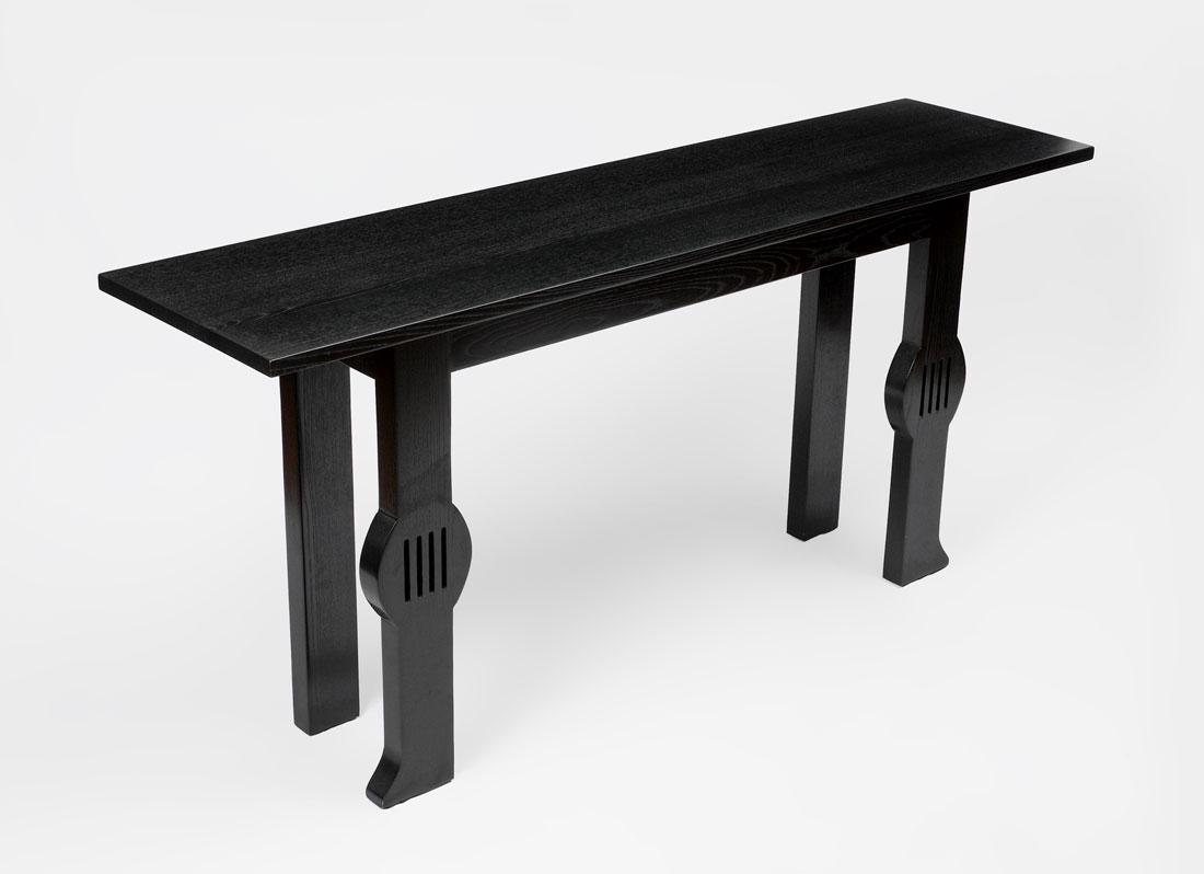 KARL SPRINGER STYLE ALTAR / SOFA TABLE: KARL SPRINGER STYLE ALTAR / SOFA TABLE: Ebonized tall altar or sofa table, legs on one side with pierced center medallion, shaped foot. Unmarked, overall measures 33 1/2" h. x 70" x 18".
