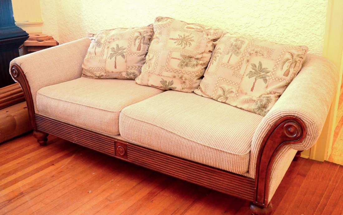 CONTEMPORARY SOFA: CONTEMPORARY SOFA: Shaped arms, carved and fluted wood front, turned legs, tan cloth fabric, three palm tree motif throw pillows. 31" h. x 86" x 36".