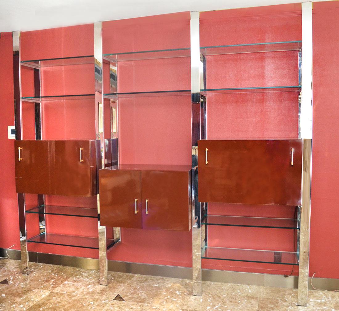 MODERNE CHROME AND GLASS WALL UNIT: MODERNE CHROME AND GLASS WALL UNIT: Unit constructs to 3 floor to ceiling sections, chrome supports, each section having a maroon lacquered cabinet and adjustable glass shelves. One cabinet with 2 doo