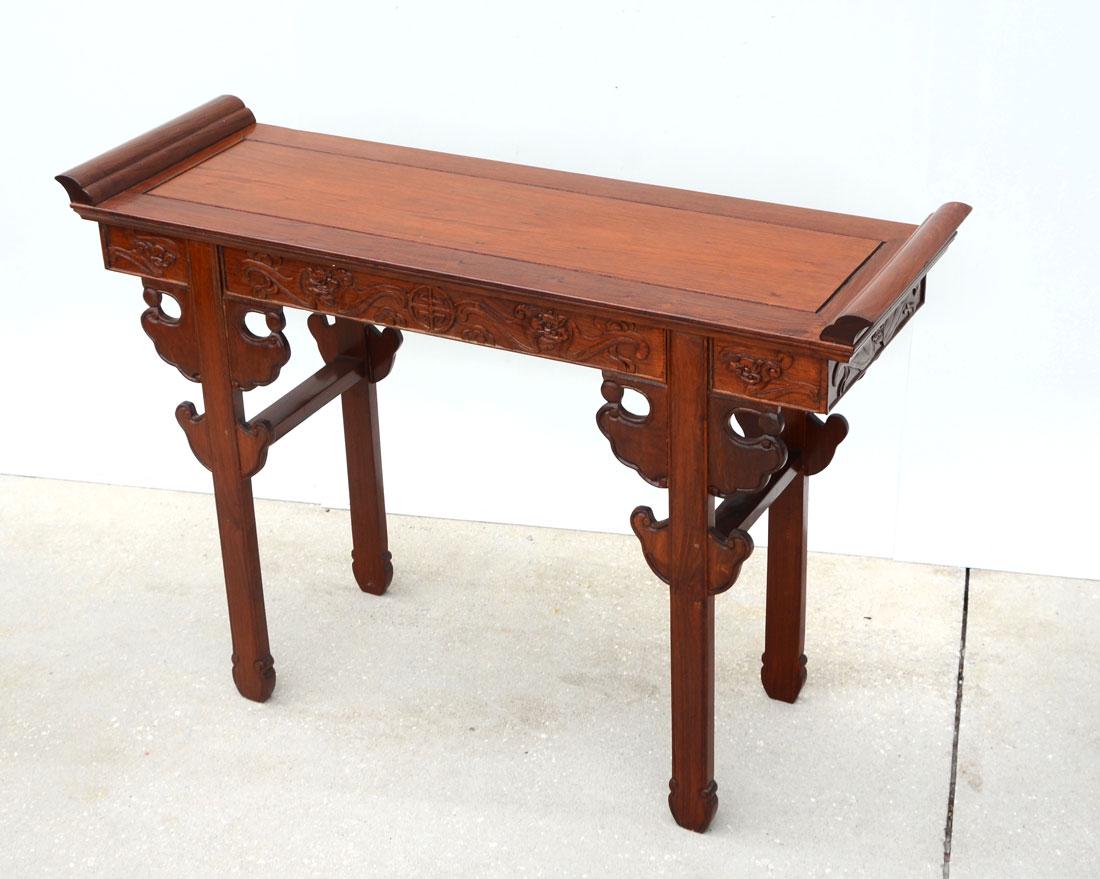 CHINESE CARVED ALTAR TABLE: CHINESE CARVED ALTAR TABLE: Top with upturned ends, carved skirt with stylized bats and dragon head, carved legs, 33'' h. x 48 1/4'' x 15 1/2''.