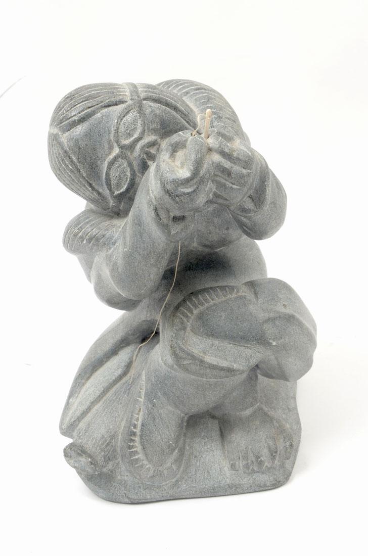 TIVI ILISITUK CARVED SOAPSTONE FIGURE: ILISITUK, Tivi, (Inuit/Canadian, 1933-2012): Carved soapstone figure of a man threading a bone needle, identification label and Canada Eskimo Art label on base, overall 9'' x 6''.