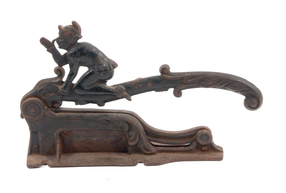LARGE CAST IRON FIGURAL JESTER CIGAR CUTTER: LARGE CAST IRON FIGURAL JESTER CIGAR CUTTER: This old Cigar cutter has a figural jester with thumb on his nose and other fingers in the air. He is sitting on a scrolling foliate designed handle. Blade