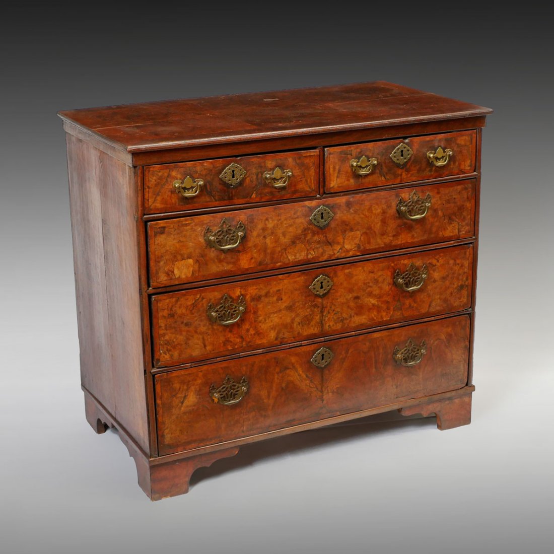 EARLY BURLWOOD VENEERED 5 DRAWER CHEST: EARLY BURLWOOD VENEERED 5 DRAWER CHEST: This veneered burlwood chest has 2 smaller drawers at top over 3 drawers. Pierced brass bail handles and pierced brass decorated key holes. Resting on ogee foot
