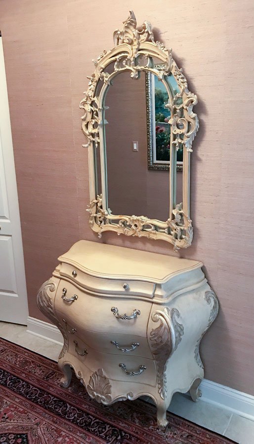 CONTEMPORARY BOMBE COMMODE AND ORNATE MIRROR: CONTEMPORARY BOMBE COMMODE AND ORNATE MIRROR: Antiqued cream and silver paint decorated commode, 4 drawers, bombe sides and front, on shaped legs. Approx. 33.25'' h. x 39.75'' l x 19' w. Sold with a r