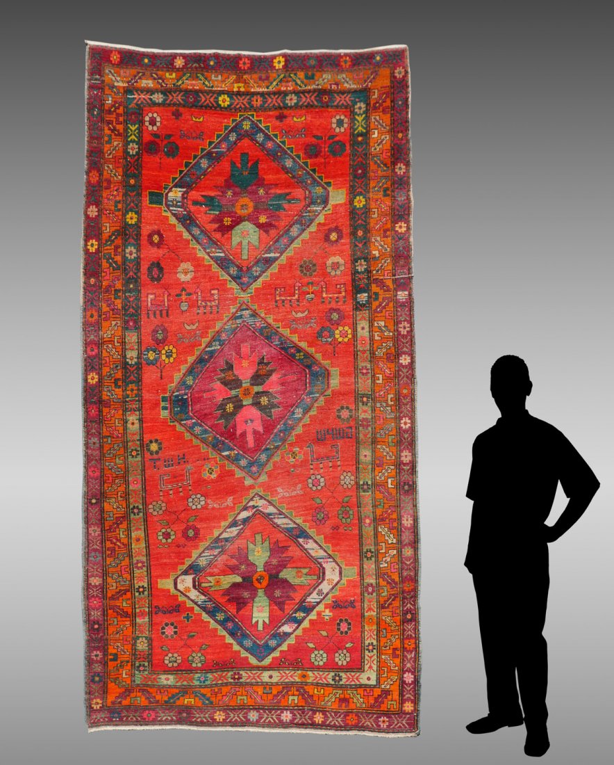 CAUCASIAN SOVIET ERA MID-CENTURY HK RUG 5'1" X 9'11": CAUCASIAN SOVIET ERA MID-CENTURY HAND KNOTTED WOOL RUG, 5'1" X 9'11": An outline diamond shaped pattern repeats down center of red/orange field. The initials T.W.H. Are in one side and a gibberish dat
