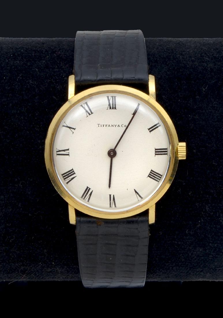 VINTAGE 14K TIFFANY ROUND CASE WRISTWATCH: VINTAGE 14K TIFFANY ROUND CASE WRISTWATCH ON BLACK LEATHER STRAP: 14K yellow gold watch with white dial, black pointed stick hands and Roman numeral hour markers. Cream color face with Tiffany & Co at