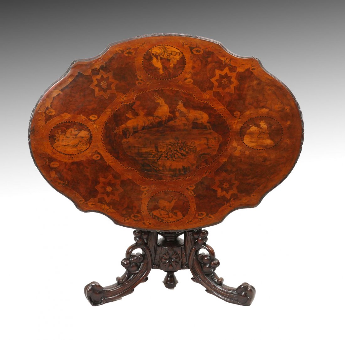 CARVED BLACK FOREST TILT TABLE: CARVED BLACK FOREST TILT TOP TABLE: Black Forest tilt-top table having inlaid mountain hunting scenes and star medallions. Carved & pierced skirt, raised on a pierced 3-legged foliate base. Approx. 29