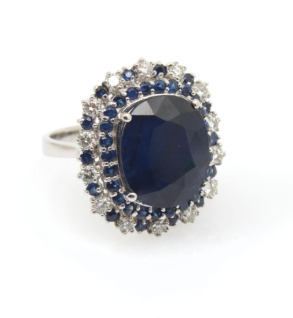 14K SAPPHIRE & DIAMOND RING: 14K SAPPHIRE & DIAMOND RING: 15.44 CT sapphire is circled by a row of small sapphires and then a row of diamonds and sapphires, all in white gold. Sapphire is oval shape and is an evenly colored dark 