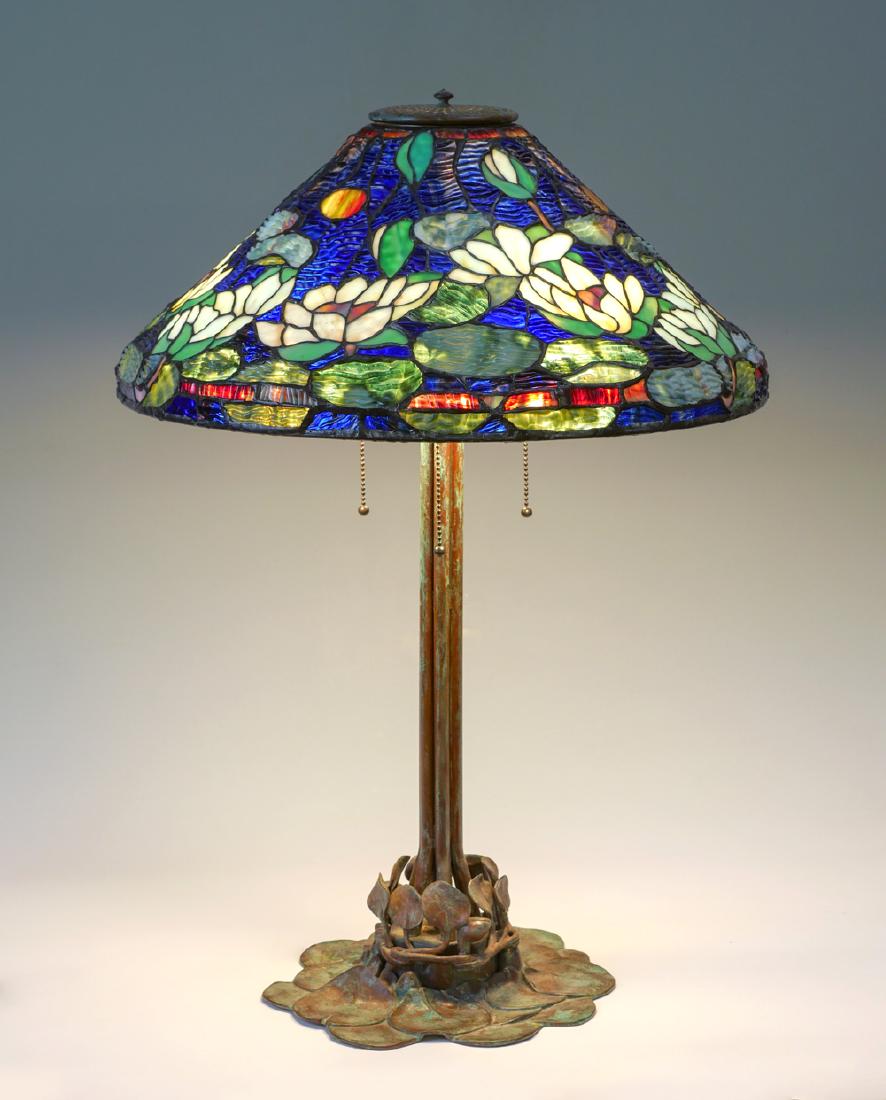 TIFFANY STYLE LEADED LILYPAD LAMP: TIFFANY STYLE LEADED LILY PAD LAMP: 3 light Tiffany style table lamp having a floral lily pad and pond motif stained glass shade. Mounted on a patinated metal lily pad base. Approx. 29" h x 20" w.