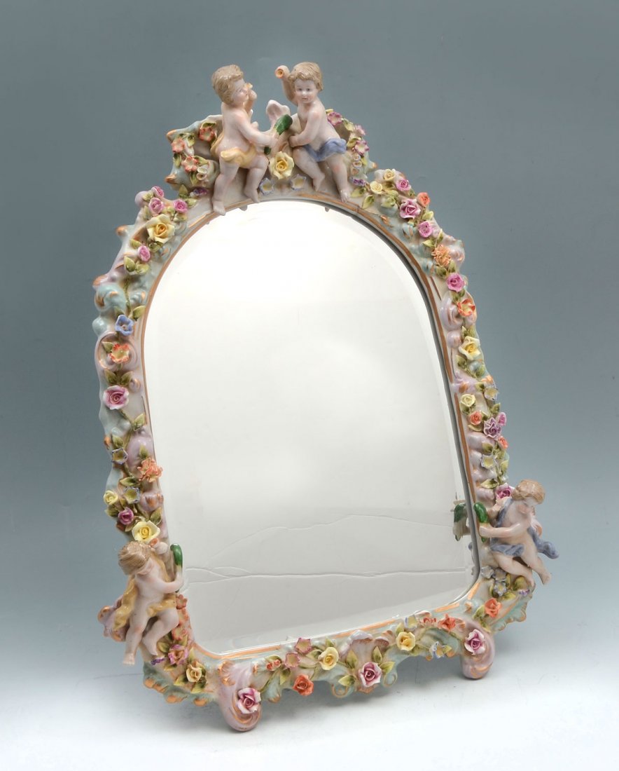 MEISSEN CHERUB MIRROR: MEISSEN CHERUB MIRROR: Meissen porcelain frame having 4 attached cherubs amongst an ornate floral & scrolling frame with a beveled mirror. Crossed sword mark resides at top right. Approx. 18.75'' h x