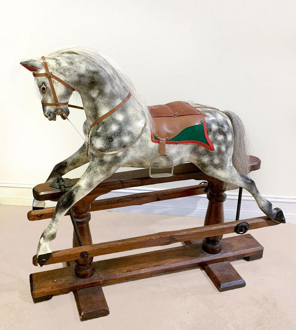 ANTIQUE ROCKING HORSE: ANTIQUE ROCKING HORSE: Carved rocking horse having a black & white body with grey hair at the mane & tail. Attached leather saddle with metal stirrups. Mounted on 2 wood rails that attach to central b