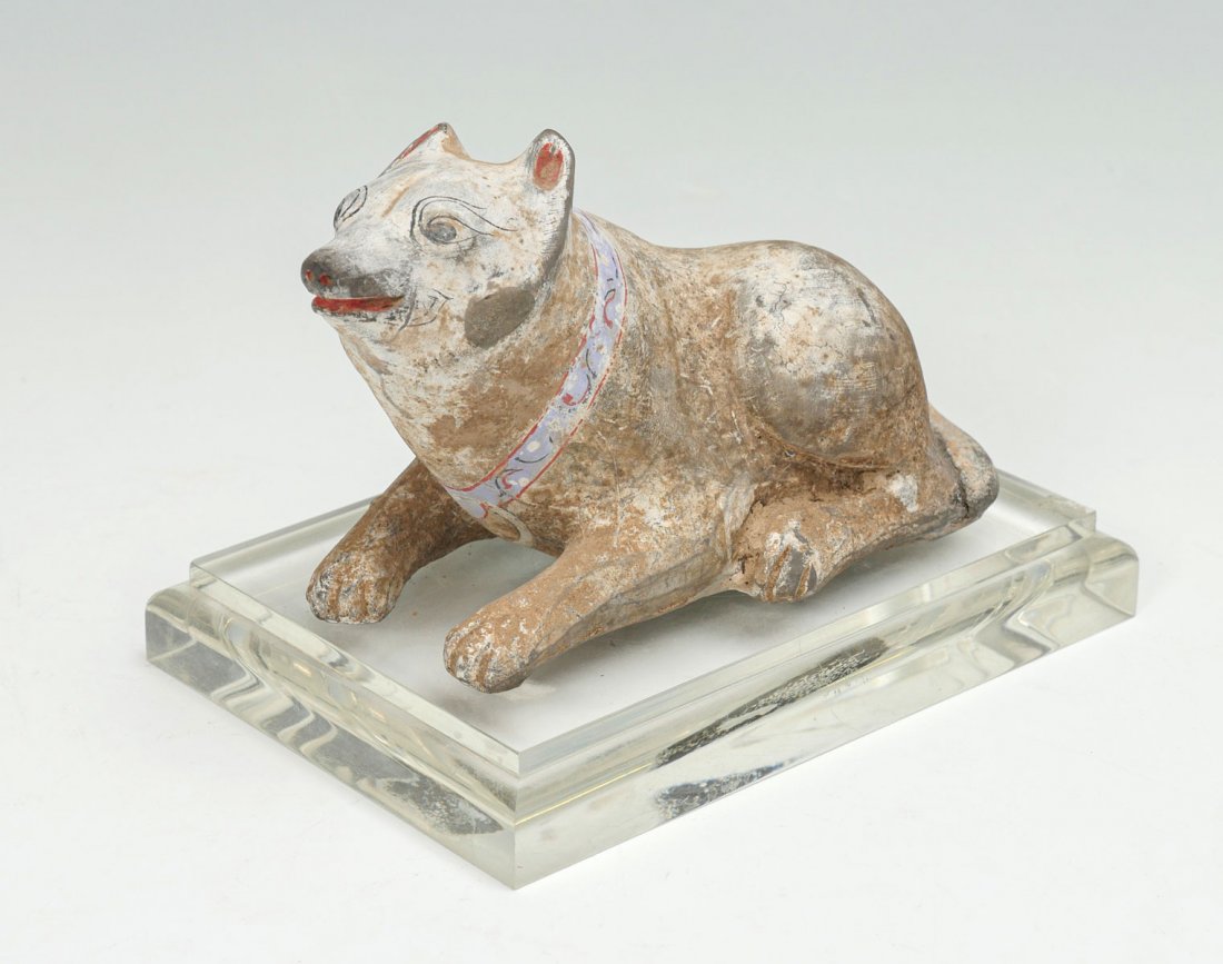 ANCIENT CHINESE HAN DYNASTY STYLE DOG SCULPTURE: ANCIENT CHINESE HAN DYNASTY STYLE DOG SCULPTURE: Chinese Han dynasty style earthenware sculpture in the form of a recumbent dog. Polychrome painted face & collar. Resting on a fitted lucite base. Appr