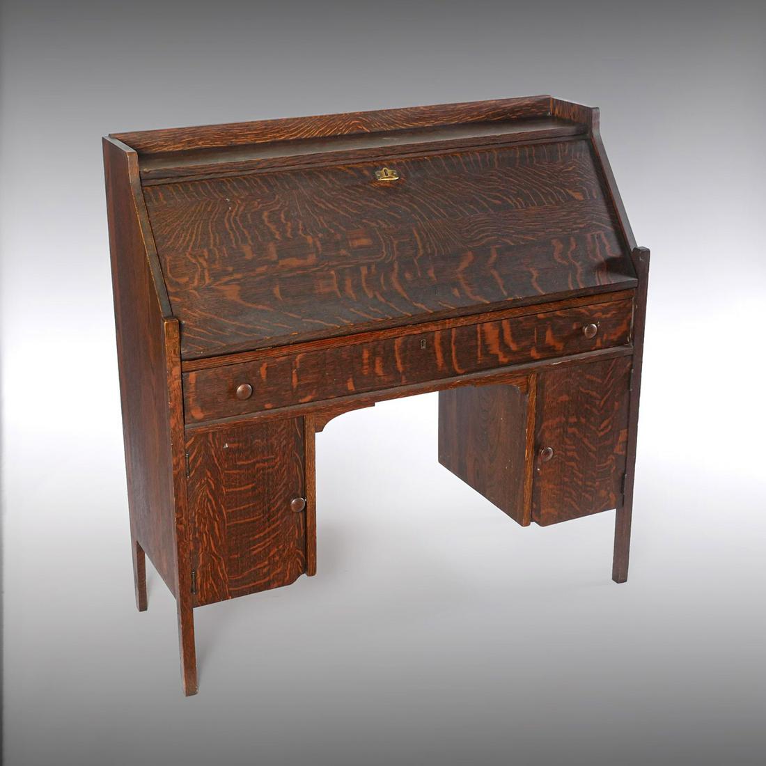 ARTS AND CRAFTS STYLE SLANT FRONT DESK: ARTS AND CRAFTS STYLE SLANT FRONT DESK: Oak slant front desk, having a compartmented interior, over a single long drawer, over 2- doors. Raised on square legs. Approx. 42.25'' h x 42'' l x 15.5'' w.