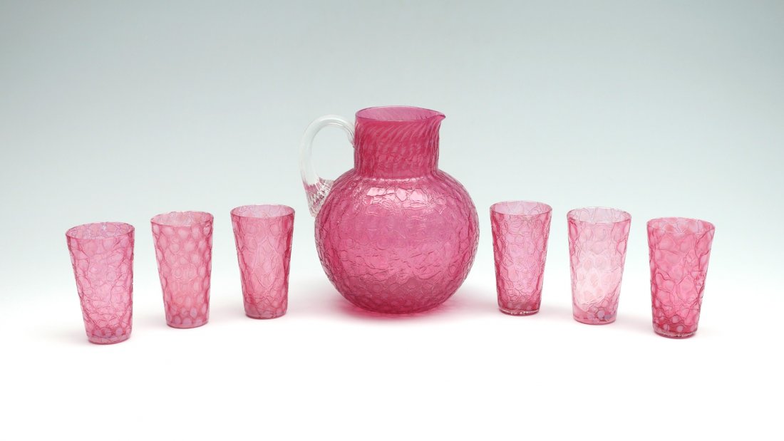 7 PIECE CRANBERRY CRACKLED DRINK SERVICE: 7 PIECE CRANBERRY CRACKLED DRINK SERVICE: Comprising; 1- Pitcher, & 6- cups. All have a Cranberry crackled body with light opalescent spots. Pitcher Approx. 7" h x 6.5" l @ handle x 6" w. Cups Approx.