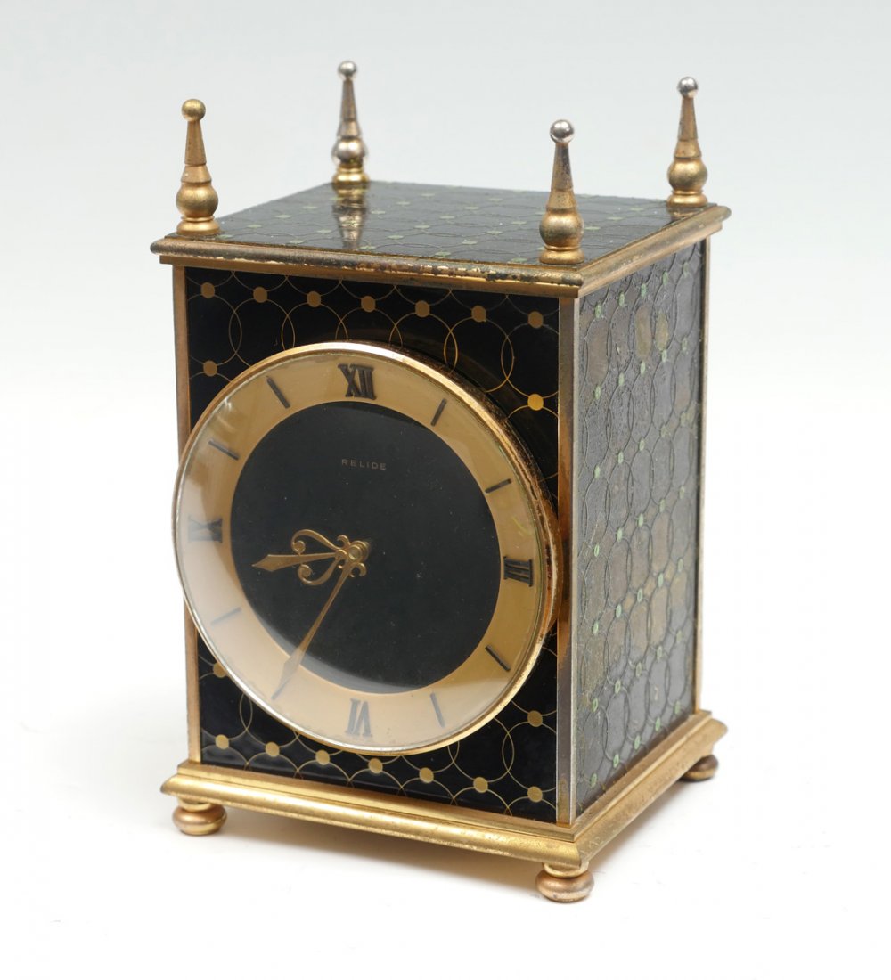 FRENCH RELIDE ENAMELED CLOCK: FRENCH RELIDE ENAMELED CLOCK: French Relide cased clock, having a gold toned frame with an encompassing intertwining design. Black enameled, Raised on bun feet. Approx. 7.75" h x 4.75" l x 5" w.
