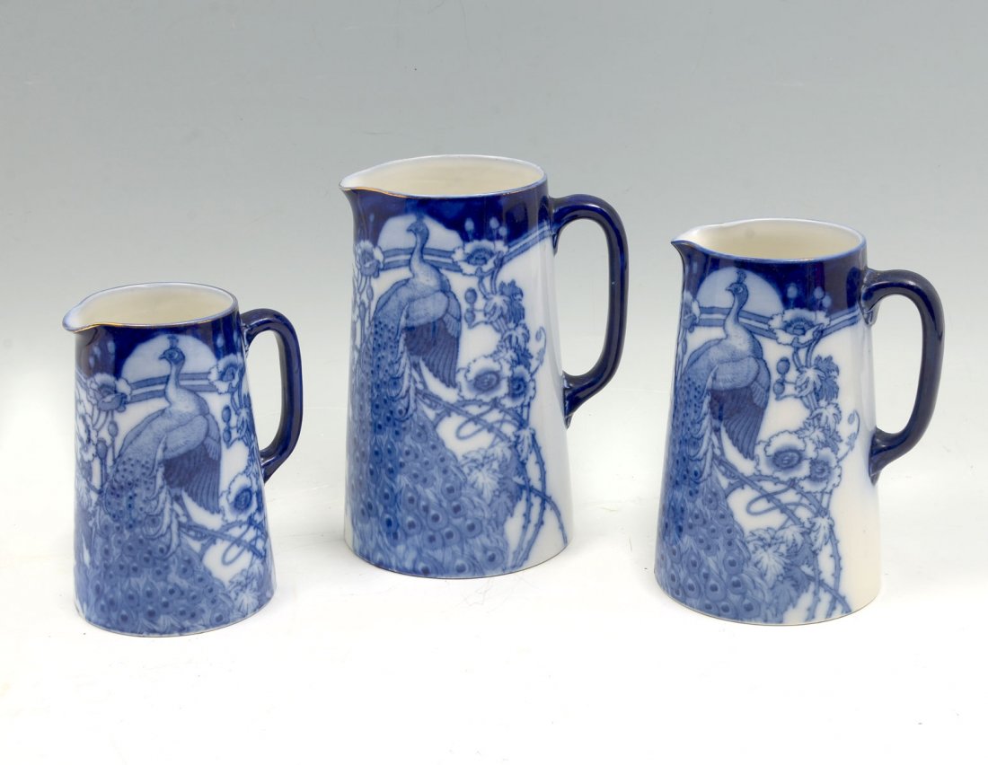 3 PC BISTO BLUE PEACOCK PITCHERS: 3 PC BISTO ENGLAND FLOW BLUE PEACOCK PITCHERS: 3- Graduated Flo Blue Bisto pitchers, having Peacocks amongst draping floral & foliate background. All signed at undersides. Largest approx. 7.75" h x 6"