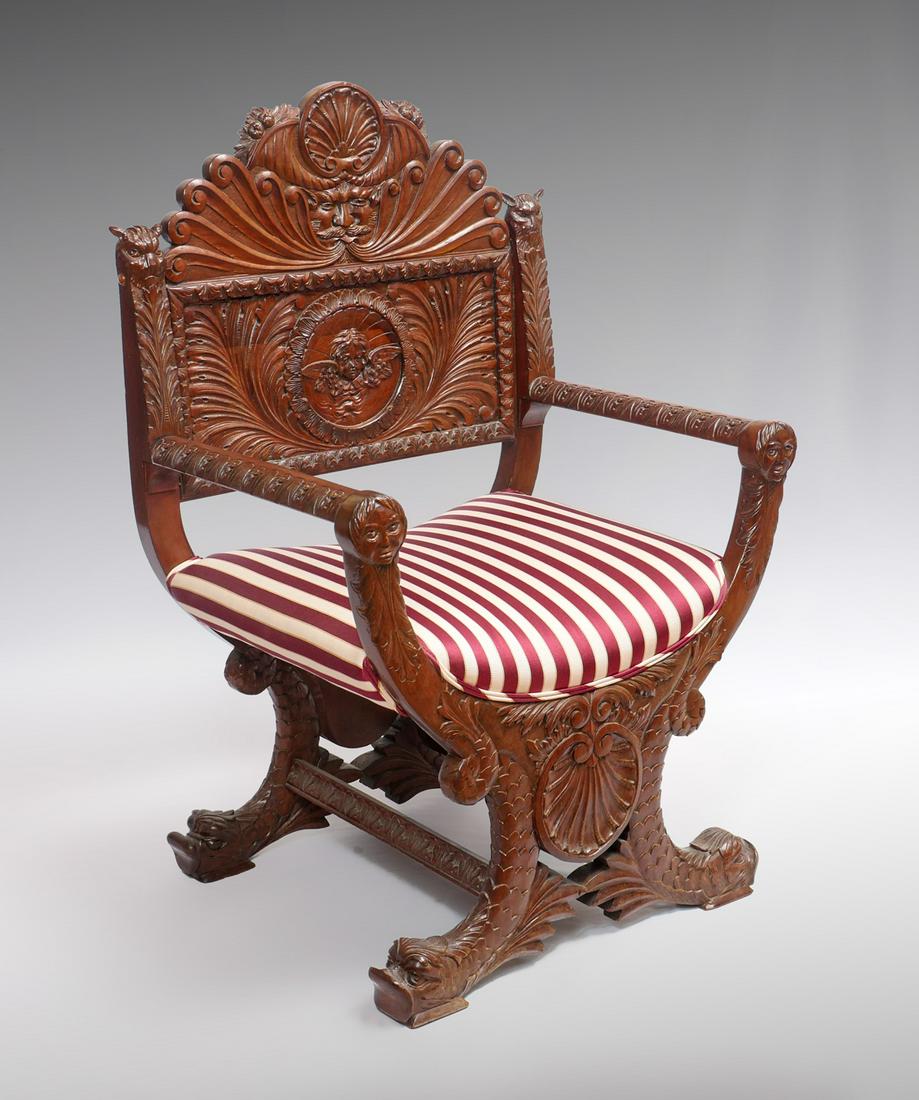 HIGHLY CARVED FIGURAL SAVRANOLA CHAIR: HIGHLY CARVED FIGURAL SAVONAROLA CHAIR: Savonarola chair having carved Shell medallions, North Wind masque, & animal faces. Dolphin Fish legs & feet. Upholstered in a striped fabric. Approx. 44.75'' h