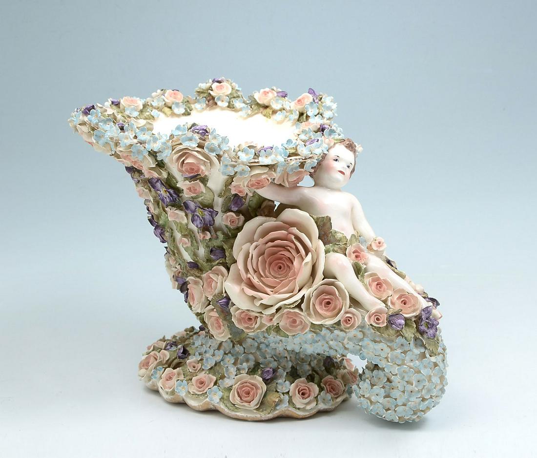 HOBE DRESDEN CORNUCOPIA: HOBE DRESDEN PORCELAIN CORNUCOPIA: Cornucopia form porcelain vase with a cherub reclining amongst attached flowers that encompass the entire piece. Hobe, Dresden mark at underside. Approx. 8'' h x 10.