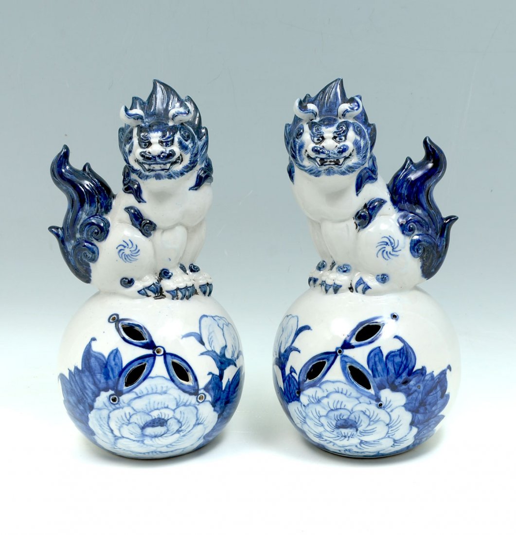 PAIR OF BLUE AND WHITE CHINESE PORCELAIN FOO DOGS: PAIR OF BLUE AND WHITE CHINESE PORCELAIN FOO DOGS: Opposing pair of Foo Dogs on a pierced ball form base with blue & white decorated floral & foliate design. Incised signature at undersides. Approx. 1