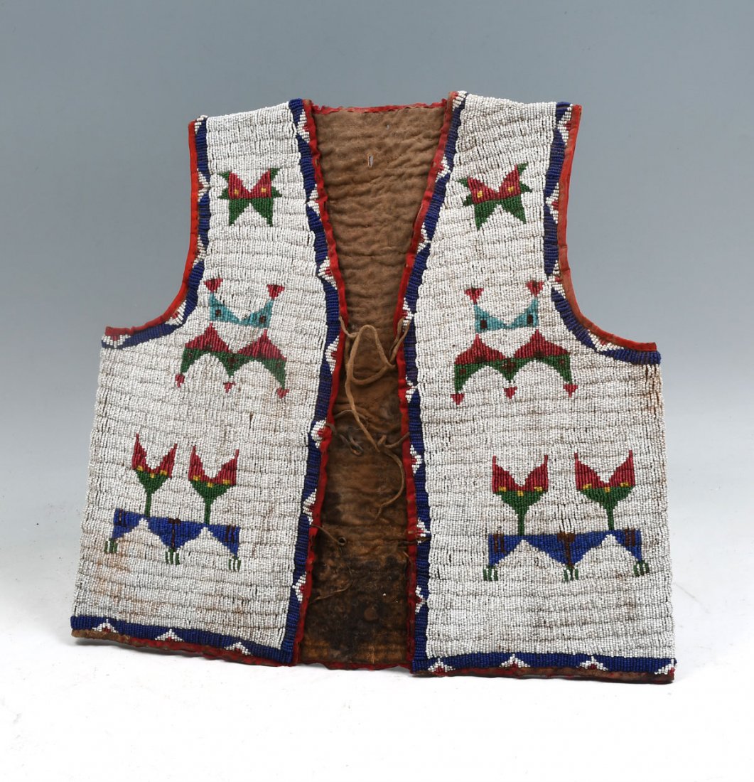 BEADED BOYS HIDE VEST: NATIVE AMERICAN INDIAN BEADED BOYS HIDE VEST: Hide vest is beaded on both sides with multi-colored geometric design on a white background. Approx 15'' long.