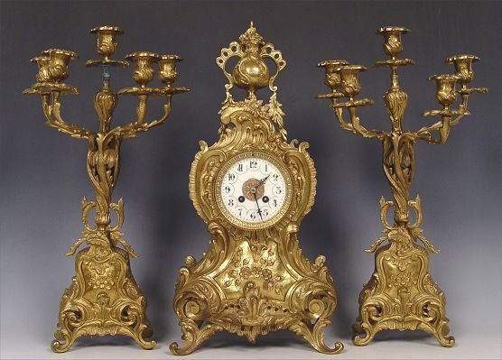 FRENCH BRONZED CLOCK GARNITURE SET: FRENCH BRONZED CLOCK GARNITURE SET: Cast bronzed metal case clock with urn finial. Porcelain dial with Arabic numerals, unsigned on face or key and pendulum mechanism. Beveled glass crystal. Measures