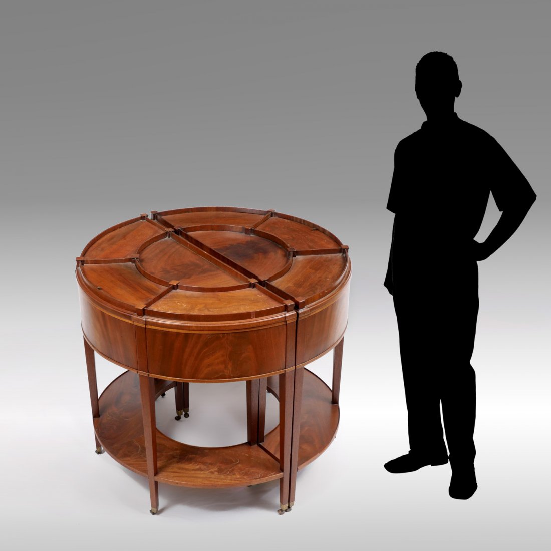 MOST UNUSUAL METAMORPHIC COMPARTMENTED DRUM TABLE: MOST UNUSUAL METAMORPHIC COMPARTMENTED DRUM TABLE: A rare mahogany Drum Table witch splits to form a pair of compartmented demilune wall tables. Raised on tapered square legs with metal casters. Toget