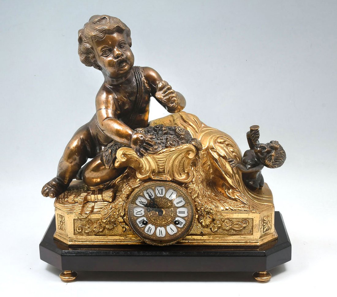 GILT METAL CHERUB CLOCK: FRANZ HERMIE AND SON GILT METAL CHERUB CLOCK: Gilt metal case with a large cherub with bouquet of roses and a smaller child figure blowing a horn. Interesting double bell strike movement. Works marked
