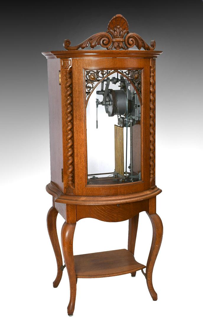 REGINA BOWFRONT UPRIGHT CHANGER MUSIC BOX: REGINA BOWFRONT UPRIGHT CHANGER MUSIC BOX: Serial #50375. Oak case with shell carved crest, spiral turned columns and curved glass front door, on a 1 drawer stand w/ snake foot cabriole legs. Plays 15