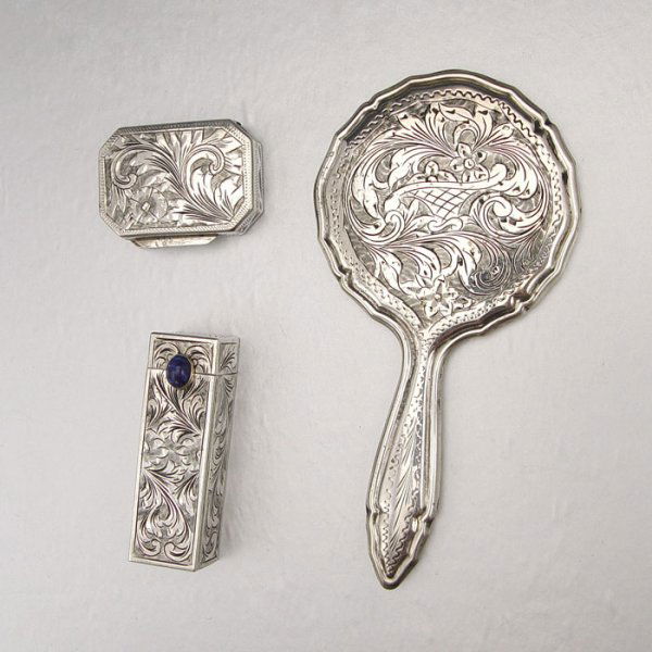 DIMINUTIVE CONTINENTAL SILVER VANITY SET: DIMINUTIVE CONTINENTAL SILVER VANITY SET: All with engraved foliate scroll design to include 1) Lipstick with blue stone cabochon, 2 1/4" l. 2) Pill box, 1 1/2". Hand mirror, 5" x 2 1/2". No makers ma