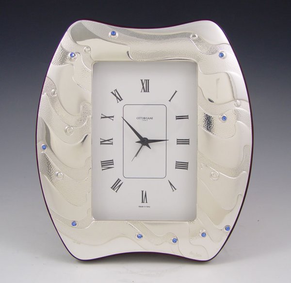 OTTAVIANI STERLING CLOCK: OTTAVIANI STERLING CLOCK: Free form design on sterling front with blue crystal accents. Marked Ottaviani, 925 and 899 ROM on front. Battery powered quartz movement. Made in Italy. 8 1/2" h. x 7 3/4" x
