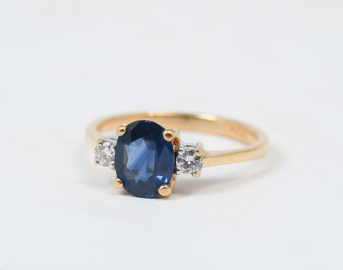 18K 1.20 CT SAPPHIRE & DIAMOND RING: 18K 1.20 CT SAPPHIRE & DIAMOND RING: 18K yellow gold ring contains 1 oval mixed cut sapphire. WEIGHT: 1.20 Ct. Approx. Rated VS in clarity (Type II), B in Hue, 6 in Tone and 3 in Saturation. 2 round b